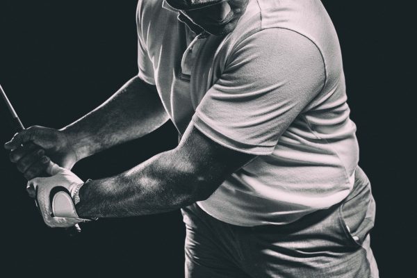 Up close black and white image of golfer swinging at a golf ball.