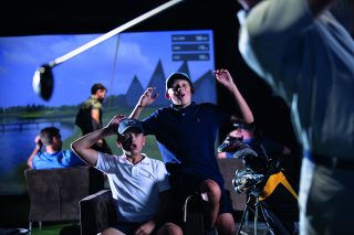 Two young golfers excited after watching another golfer take an impressive shot on the simulated green.